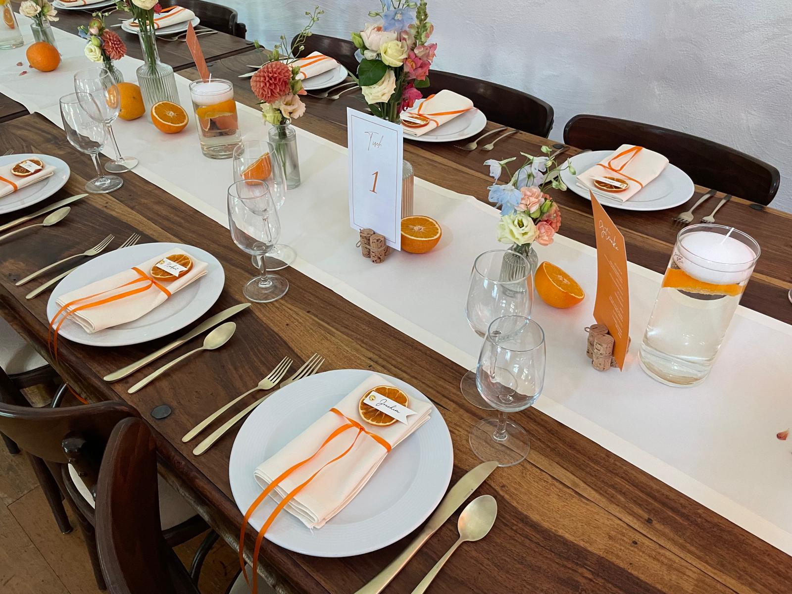 Festlich gedeckte Hochzeitstafel mit orangefarbenen Details, Blumen und handgefertigten Orangenscheiben als Namensschilder